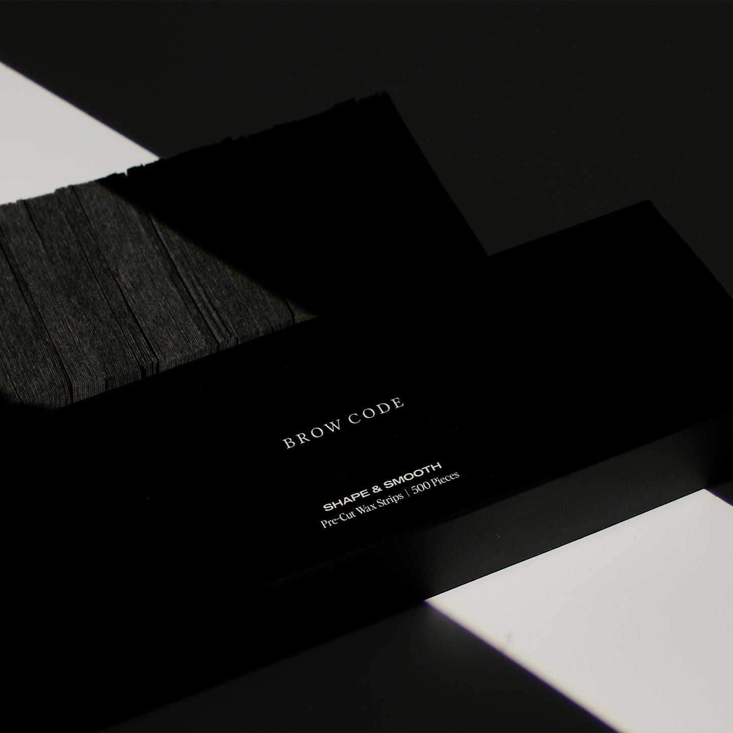 Brow Code's Pre-Cut Wax Strips packaging displayed beside a set of the pre-cut wax strips, showing both the product and its outer packaging