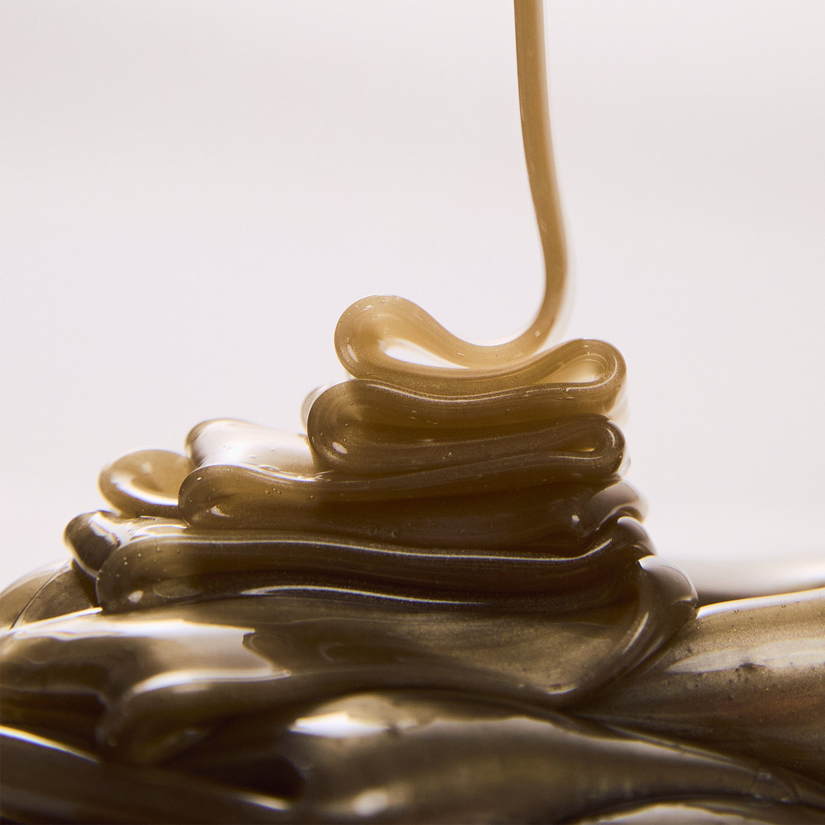 Close-up of a stream of Brow Code's Butter Bond wax being poured into soft, glossy folds on a light background