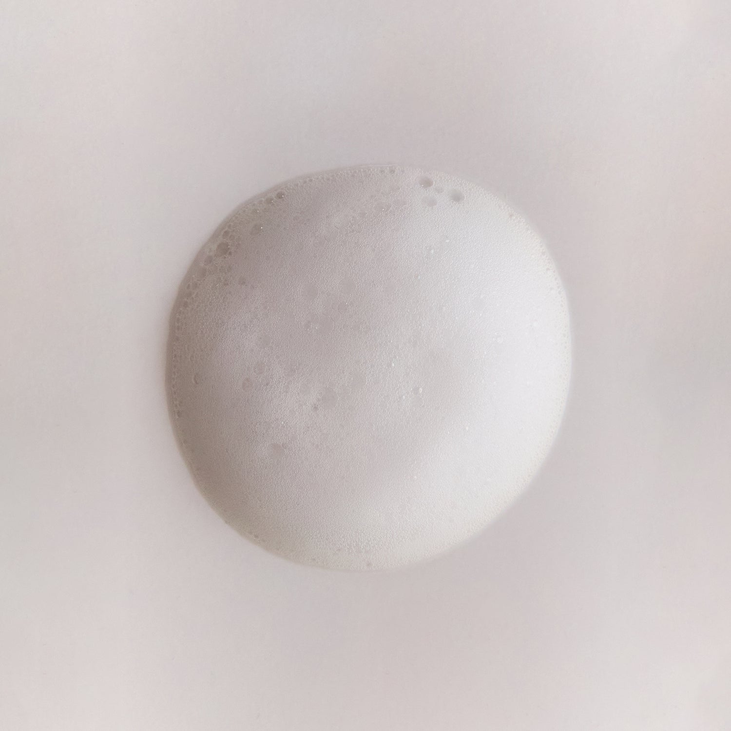 Close-up of a round mound of white foam with fine bubbles on a soft, neutral background