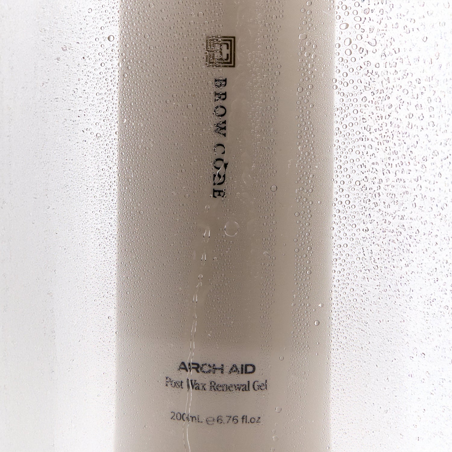 Brow Code Arch Aid Post Wax Renewal gel bottle behind a foggy, wet surface