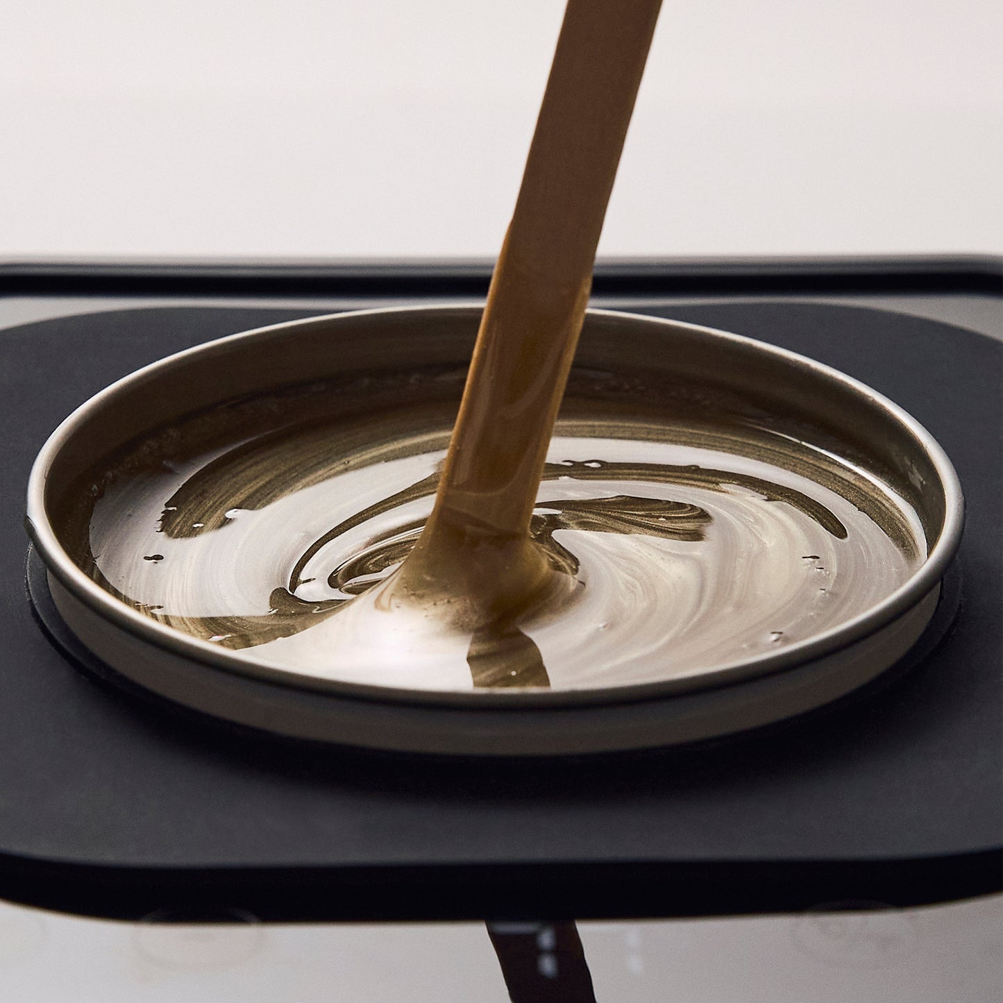 Close-up of Brow Code's Butter Bond wax being drizzled into a heated wax pot. The golden-brown wax has a smooth, creamy consistency