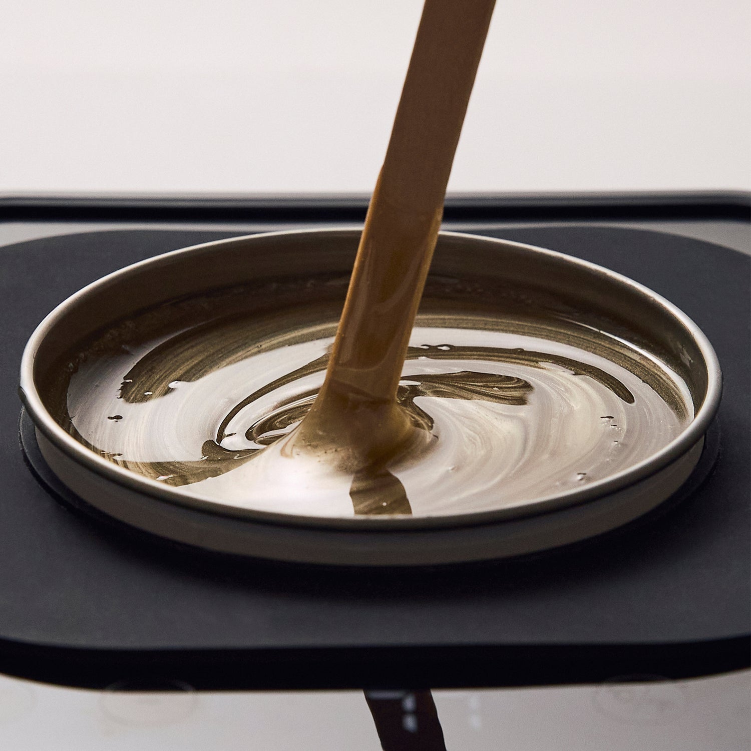 Close-up of Brow Code's Butter Bond wax being drizzled into a heated wax pot. The golden-brown wax has a smooth, creamy consistency